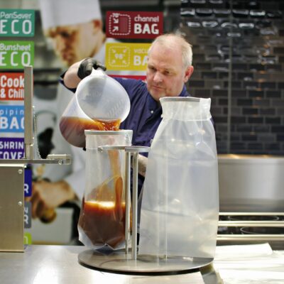 Mann füllt heiße Speisen in einen Cook & Chill Beutel mit Abfüllstation in einer Profiküche.