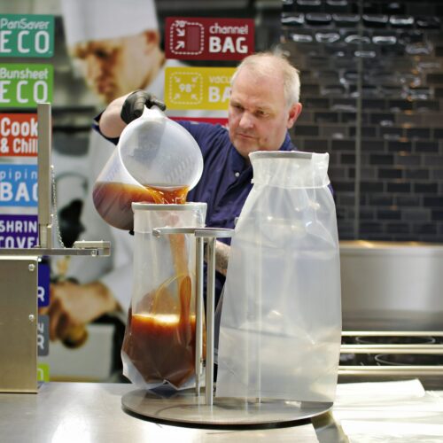 Mann füllt heiße Speisen in einen Cook & Chill Beutel mit Abfüllstation in einer Profiküche.